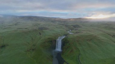Güneşin doğuşuyla İzlanda 'nın engin yeşil alanlarını, sis içindeki uzak dağları, ünlü Skogafoss Şelalesi, İzlanda çevresinde sakin ve gizemli bir atmosfer yaratıyor. Skogar 