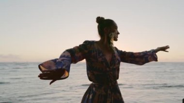 Gün batımında okyanusun kenarında zarif bir şekilde dans eden bir kadın şık, akıcı bir elbiseyle süslenir. Sahilde huzur dolu ve huzurlu bir anı yakalıyor. Güzelliği ve özgürlüğü çağrıştırıyor.