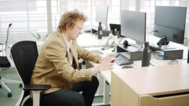 Bilgisayarlar ve ofis araçlarıyla çevrili genç bir işadamıyla modern bir ofis ortamı, profesyonellik ve odak yayıyor, refah dolu ve verimli bir çalışma alanı gösteriyor