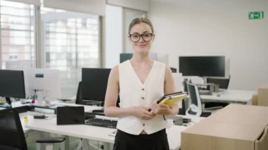 Modern bir şirket ofisinde, kendine güvenen genç bir kadın bilgisayar ve ofis aksesuarları ile çevrilidir, girişimci ve yenilikçi bir çevreyle takım çalışmasını ve verimliliğini teşvik eder.