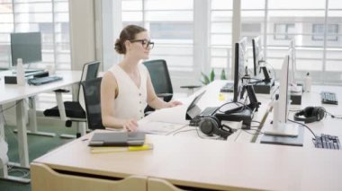 Çağdaş bir ofisteki sahne bilgisayarlarla ve evrak işleriyle uğraşan genç bir iş kadınını içeriyor. Bu bir yenilik, işbirliği ve profesyonellik ortamı.