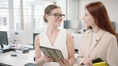 Farklı geçmişlere sahip iki çalışan modern bir ofiste dijital tablet kullanarak iş görüşmeleri yapıyorlar. İşbirliği ve iletişime odaklandılar.