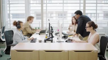 Modern bir ofiste, çeşitli bir ekip şirket hedeflerine ulaşmak, takım çalışmalarını, yenilikleri ve çoklu görevleri vurgulamak için tartışmalar, bilgisayar görevleri ve belge incelemeleri üzerinde birlikte çalışır.