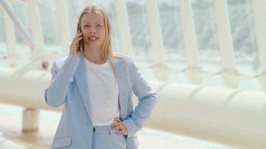 Açık mavi takım elbiseli kendine güvenen bir iş kadını, modern bir kentsel iş yerinde aktif bir telefon görüşmesi yapıyor. Bu kurumsal ortamda profesyonellik ve tarz yayıyor.
