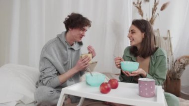 Işıl ışıl bir yatak odasında, genç bir çift rahat bir şezlong giyerken yulaf ve elmanın tadını çıkararak yatakta kahvaltıdan zevk alır. Romantik ve samimi bir ortamda birlikteliklerini paylaşıyorlar.