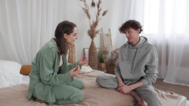 Genç bir çift, doğal dekor aksanlı, minimalist bir yatak odasında yatakta sohbet ediyor..