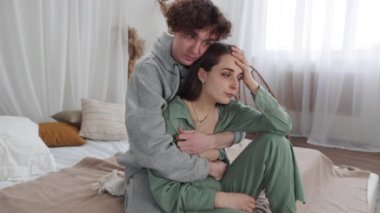 Duygusal bir anda bir çift, biri diğerini evinde rahatlatıyor, sıcak bir yatakta destek ve bakım gösteriyor.