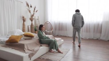 Minimalist yatak odası, pijamalı modern bir çift, doğal dekorla çevrili ilişkiler hakkında samimi tartışmalar.