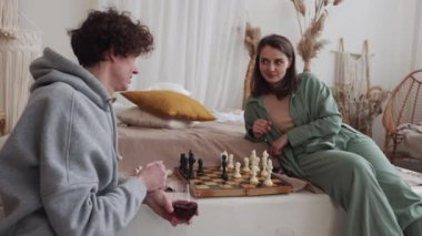 Genç bir çift, rahat evlerinde satranç oynarken birbirlerine eşlik ederek eğleniyorlar.