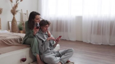 Bir çift yerde oturur, bir kadeh şarap içerler ve rahat, doğal bir ışık ayarında akıllı bir telefonla meşgul olurlar..