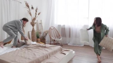 Minimalist yatak odası ortamında neşeli bir yastık kavgasına tutuştular, neşe ve eğlence anları yakaladılar..