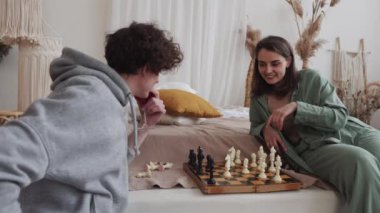 Genç bir çift rahat bir apartman dairesinde satranç oynuyor, rahat kıyafetler ve sıcak bir atmosferi var..