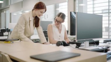 Modern ofis ortamında iş birliği yapan iki başarılı genç iş kadını. Masaüstü bilgisayarlarını kullanırken iş ve fikirleri tartışıyorlar. Çeşitli, kurumsal ortak çalışma sahneleri.