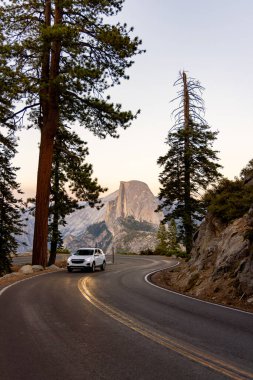 Yosemite Milli Parkı 'ndan geçen güzel, dolambaçlı bir yol. Etrafı ağaçlarla çevrili ve güneş doğarken nefes kesen dağ manzaralarıyla çevrili.