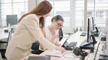 Çağdaş bir ofiste profesyonel kadınlar işbirliği yapıyor, belgeleri tartışıyor ve bilgisayar üzerinde çalışıyor, şirket ortamında takım çalışmasının ve verimliliğin önemini vurguluyorlar.