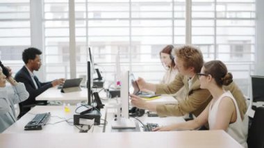 Modern bir ofis ortamında, hırslı genç profesyonellerden oluşan çeşitli bir ekip yenilik ve etkili iletişim ve takım çalışması yoluyla iş başarısı elde etmek için teknolojiyi kullanarak işbirliği yapıyor.