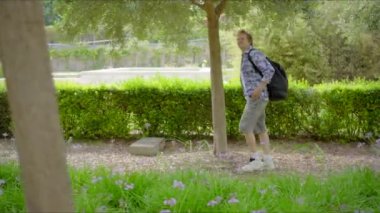 Genç bir adam canlı bir parkta yürüyor, akıllı telefonuyla mesajlaşmaya kendini kaptırmış, teknolojinin ve doğanın güzelliğini yemyeşil ve renkli çiçekler arasında somutlaştırıyor.