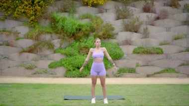 Atletik ve enerjik bir kadın fevkalade canlılığını ve sağlığını gururla sergiliyor. Canlı, renkli bir minder üzerinde yoga yaparak, ki bu da ilham verici doğal bir zemine karşı güzelce hazırlanmıştır.
