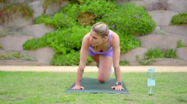 Kendini adamış ve tutkulu bir fitness kadını, açık havada yoga minderi üzerinde gayretle çalışıyor. Etkileyici atletizmini ve sağlık, sağlık ve sağlık konusundaki değişmez bağlılığını açıkça gösteriyor.
