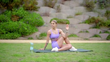 Barışçıl bir açık hava ortamında, kendine güvenen bir kadın yoga uygulamasına dalıp atletizmini ve spor, sağlık ve refahını gösterir.