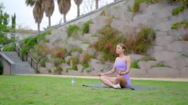 Barışçıl bir açık havada, genç ve atletik bir kadın minderinde yoga yapıyor, sadece gücünü ve güzelliğini göstermiyor, aynı zamanda sağlığını ve canlılığını da arttırıyor.