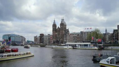 AMSTERDAM, NETHERLANDS - 11 Nisan 2023 Amsterdam 'ın büyüleyici bir manzarası yumuşak bir gökyüzünün altındaki sakin sularda tarihi binalar ve zarif tekneler, şehrin büyüleyici atmosferini yakalıyor. 