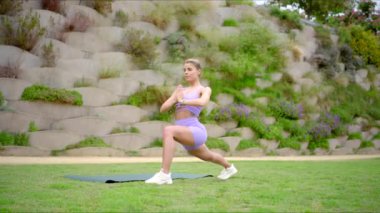 Güçlü, güzel bir kadın, doğa manzaralı bir ortamda yoga minderinin üzerinde atletizm ve spora olan bağlılığını sergiliyor.