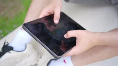 Genç adamın elleri rahat bir şekilde dışarıda otururken, modern teknolojinin gündelik ortamdaki inanılmaz etkisini etkili bir şekilde gösteren bir tablet kullanmaya odaklanmış.