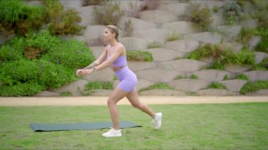 Manzaralı bir açık hava ortamında sağlıklı bir kadın yoğun egzersiziyle atletizmini ve sağlıklı bir yaşam tarzına olan bağlılığını göstermek için yoga minderinin üzerinde enerjik bir şekilde egzersiz yapar.
