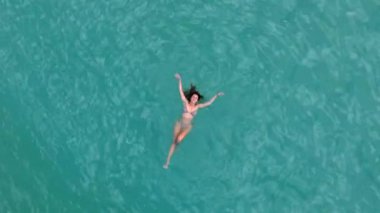 Havadan çekilen bir görüntü, Oahu, Hawaii 'nin sakin turkuaz sularında yüzen bir kadını canlı bir günbatımına karşı yüzdürür, huzur ve doğanın büyüleyici güzelliğini gösterir.