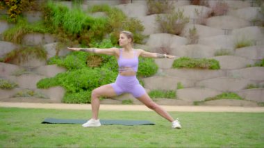 Tutkulu genç bir kadın, atletizm ve adanmışlığını açık hava yoga seanslarıyla gösteriyor. Canlı, dingin, yemyeşil bir ortamda zindeliğe olan bağlılığını gösteriyor.