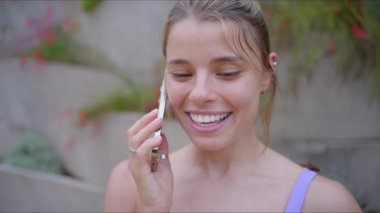 Neşeli genç bir kadın enerji dolu bir telefon görüşmesi yaparken saf mutluluğu yayar. Çevresindeki nefes kesen açık hava manzarası arasında spor ve sağlığa olan güçlü bağlılığını gösterir.