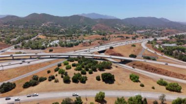 Bu görüntü, Los Angeles, Kaliforniya 'da geniş banliyö manzaraları ve nazikçe yuvarlanan tepelerle çevrili hareketli ve yoğun bir otoyol gösteren bir hava görüntüsü yakalıyor.