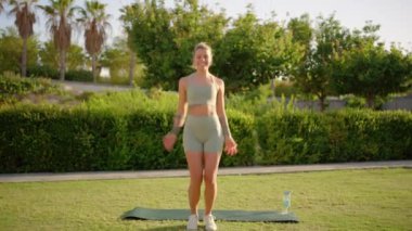 Canlı genç bir kadın, güneşli bir açık havada yoga minderiyle egzersiz yapıyor atletizmini ve sağlıklı bir yaşam tarzına olan bağlılığını gösteriyor ve başkalarına da benzer alışkanlıkları benimsemeleri için ilham veriyor.