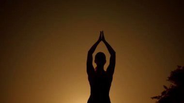 Neşeli kadın figürü, çarpıcı bir günbatımı arkaplanı önünde zarif bir yoga pozu veriyor. Bu an, günlük yaşamda zindelik, huzur ve sükunetin özünü mükemmel bir şekilde temsil ediyor.