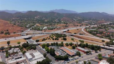 Los Angeles banliyösünde bir otoyol kavşağının havadan perspektifi, manzaralı tepelerin ortasındaki trafik akışını gösteriyor.