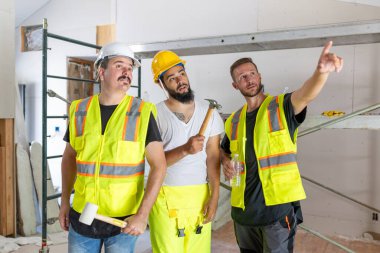 Bu canlı sahnede, güvenlik donanımlı bir mimar da dahil olmak üzere çeşitli inşaat işçileri, takım çalışmalarını ve profesyonelliklerini sergiledikleri bir ev yenileme projesinde yer alıyorlar.