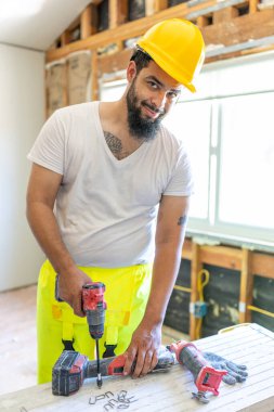 Neşeli ve hevesli bir inşaat işçisi, canlı bir yelek ve sağlam bir şapka giyer, etkin bir şekilde bir evi yeniliyor, etkileyici araç gereçlerini, becerilerini ve uzmanlığını gururla sergiliyor