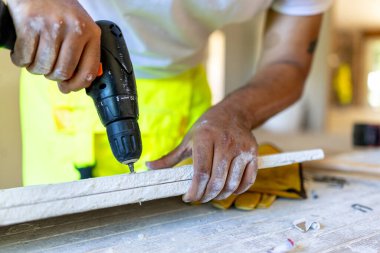 Kendini işine adamış bir inşaat işçisi, ahşap malzemeler üzerine ustalıkla bir matkap kullanarak, evin yenilenmesi ve yenilenmesi sürecinde dikkate değer bilgi ve beceri gösteriyor.