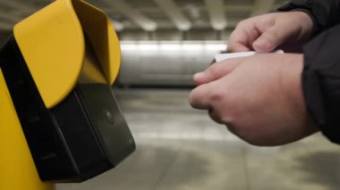 Bir kullanıcı, modern bir aktarma istasyonunda gelişmiş bir bilet doğrulama makinesine bağlanır ve günlük hayatta kentsel hareketliliğin ve ileri teknolojinin kesişimini vurgular.