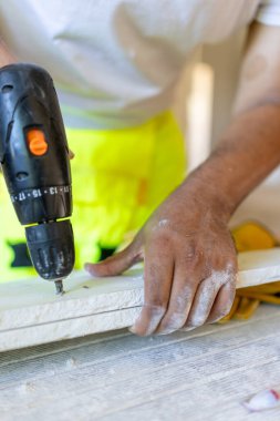 Kendini işine adamış bir erkek inşaat işçisi, evi yeniden dekore etmek için elektrikli matkap kullanıyor. Parlak güvenlik teçhizatı takıyor ve bu da onun mükemmelliğe olan bağlılığını vurguluyor.