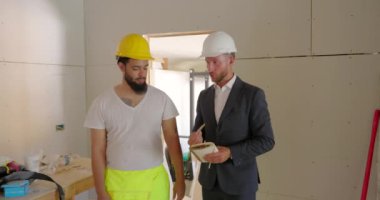 Güvenlik teçhizatı içinde bir mimar ve bir inşaat işçisi yaratıcı fikirlerini hayata geçirmeyi amaçlayan bir ev yenileme projesinde işbirliği hakkında heyecanlı bir şekilde tartışıyorlar.