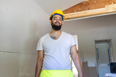 Yansıtıcı güvenlik yeleği ve sağlam bir miğfer giyen neşeli bir inşaat işçisi, yüksek seviyede profesyonellik göstergesi olan bir ev yenileme projesiyle hevesle meşgul.