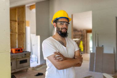 Parlak güvenlik kaskı takmış motive olmuş bir erkek inşaat işçisi, güvenlik standartları ve kalite işçiliğine olan bağlılığını gösteren, tadilat alanında gururla duruyor.