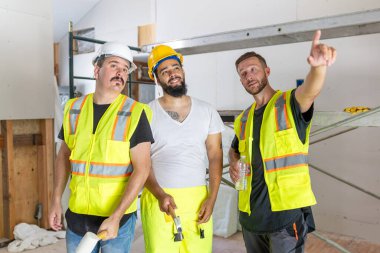 Canlı bir inşaat sahasında, güvenlik yelekleri ve kasklı üç işçi bir ev yenileme projesinde işbirliği yaparak takım çalışmasını ve bağlılığını sergileyerek hoş bir atmosfer yarattılar.