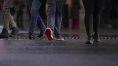 Canlı bir şehir sahnesinde yayalar yağmurlu bir caddeyi gece geçerler. Dinamik hareket ve yansımalar, çağdaş şehir yaşamını hatırlatan canlı bir şehir atmosferi yaratıyor.