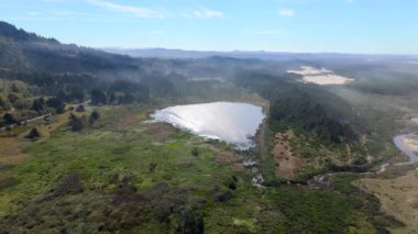 Göz kamaştırıcı hava manzarası Oregon kıyı şeridini yakalıyor. Yoğun, yemyeşil ormanları ve dingin gölü aydınlatıyor. Hepsi güzel bulutlu bir gökyüzünün altında.