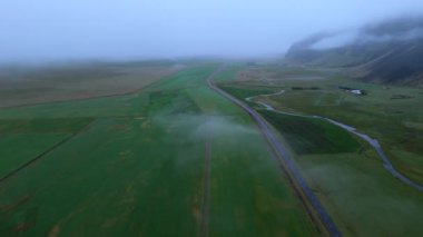 Göksel bir sis, İzlanda 'nın canlı yeşil tarlalarını çevreleyen ve doğadaki yalnızlığı ve yolculuğu sembolize eden dolambaçlı bir yol ile örtüyor. İzlanda. 