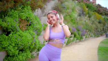 Canlı bir açık hava ortamında, neşeli bir fitness meraklısı, şık kulaklıklar takıyor, enerjik bir şekilde dans ediyor, atletizm ve spor tutkusu ve sağlıklı bir yaşam tarzı sergiliyor.
