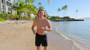 Kişi, Hawaii 'de kumlu bir plajda enerjik bir şekilde koşuyor, sıcak güneşin ve serin esintinin tadını çıkarıyor. Unutulmaz bir macera ve rahatlama tatili için mükemmel bir ortam.